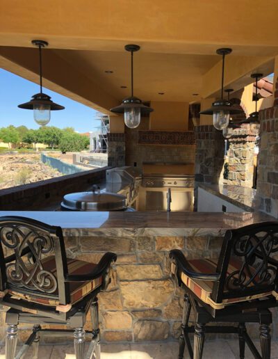An outdoor kitchen with stools and a grill.